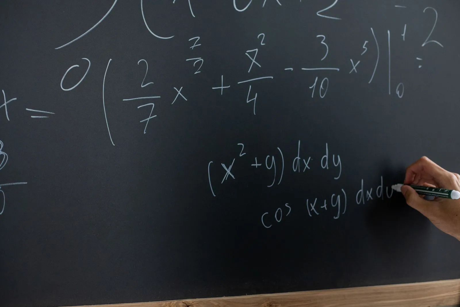 Mão escrevendo equações matemáticas com giz num quadro-negro